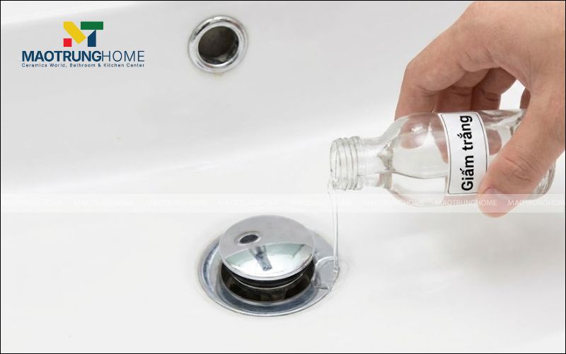 Đổ từ từ một ít giấm trắng hoặc dung dịch tẩy cặn nhẹ xung quanh khe hở của nắp nhấn